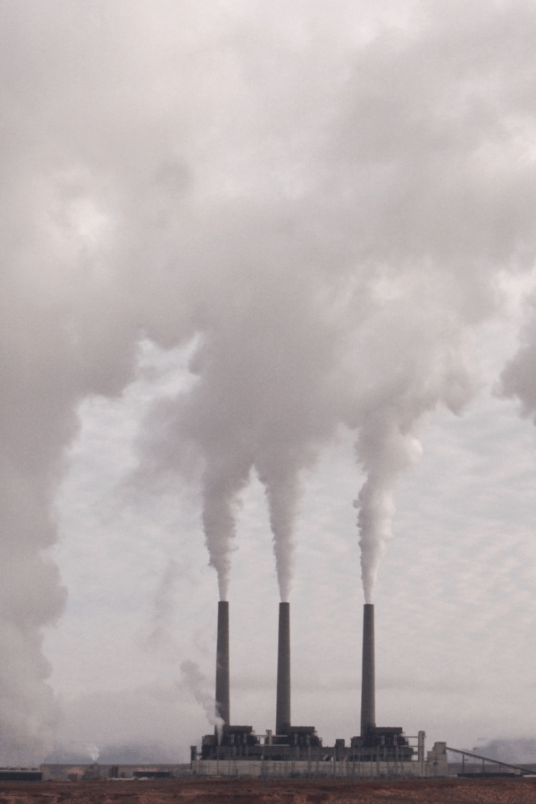 Three industrial smokestacks releasing thick white emissions into the sky.