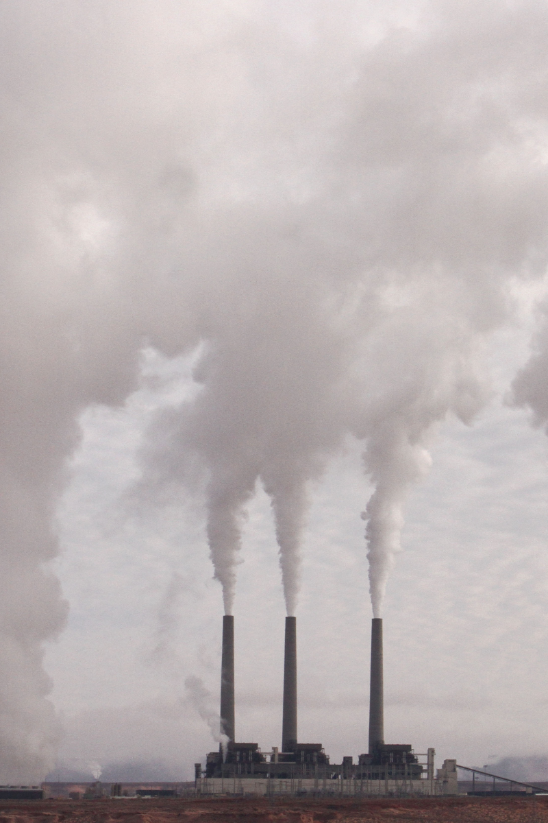 Three industrial smokestacks releasing thick white emissions into the sky.