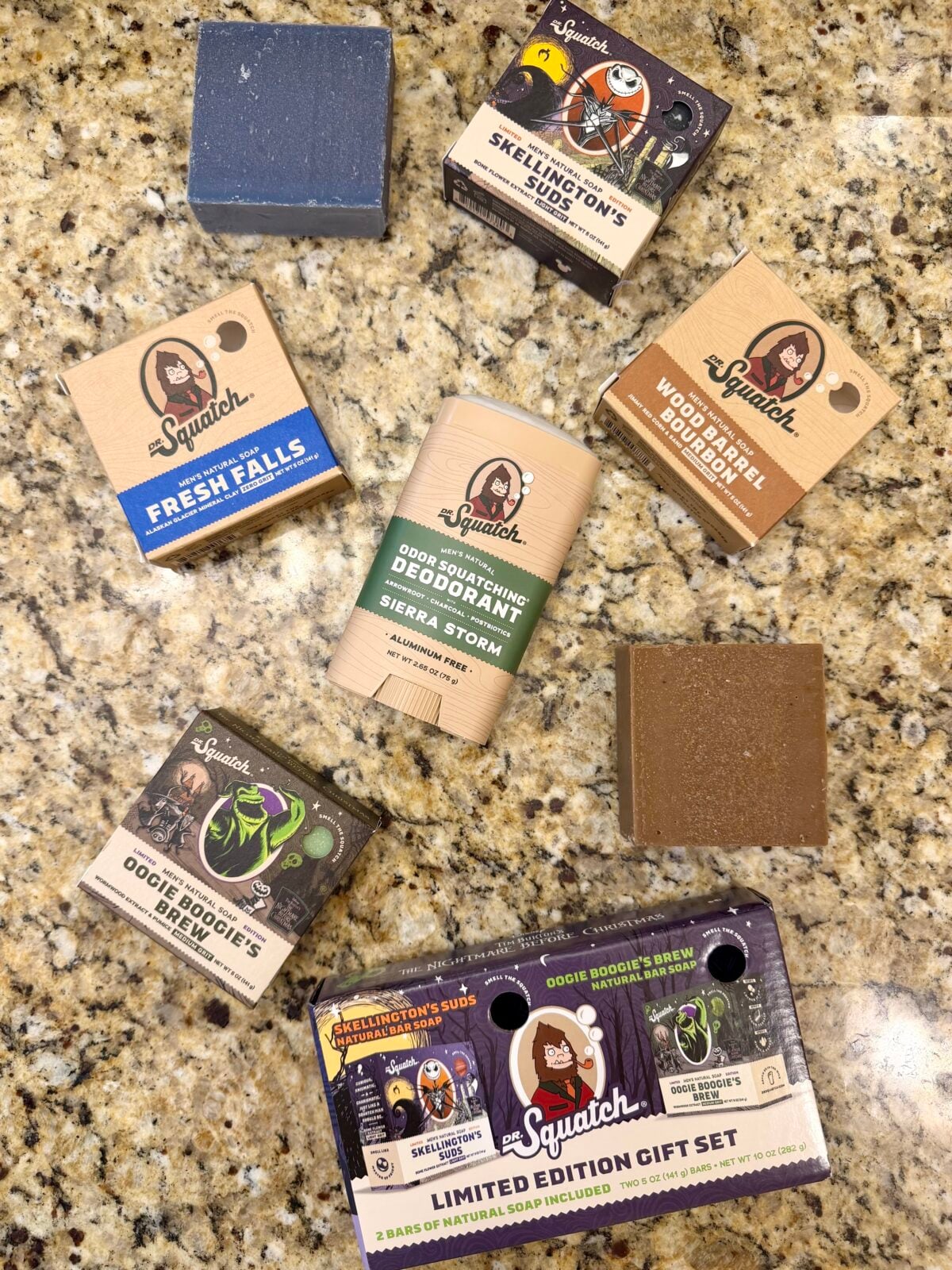 Flat lay of Dr. Squatch men’s soap bars and an aluminum-free deodorant in assorted scents, with boxed packaging and unwrapped bars on a granite countertop.