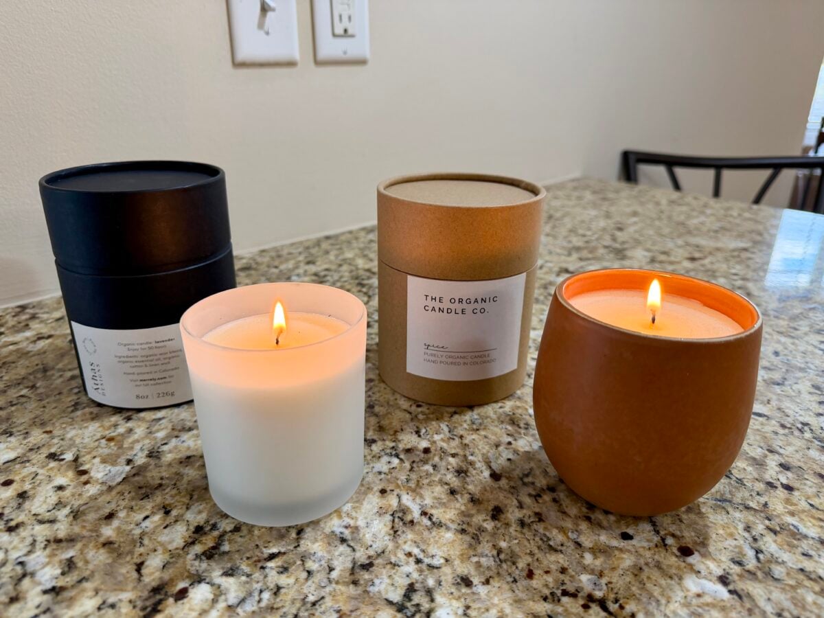 Three minimalist candles on a granite countertop, two lit, with their packaging displayed behind them.