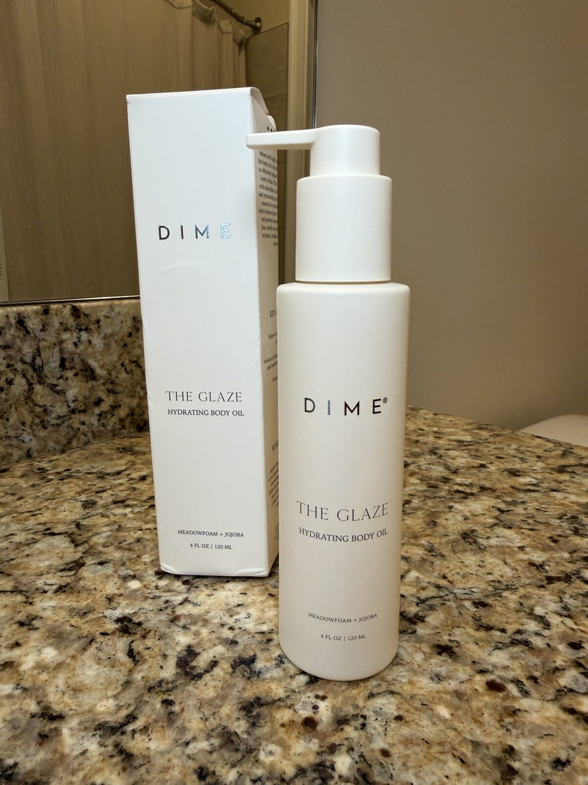 DIME The Glaze Hydrating Body Oil in white pump bottle with matching white box on granite counter