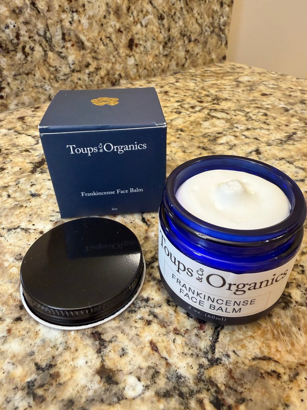 Toups & Organics Frankincense Face Balm in blue glass jar with navy box on granite counter