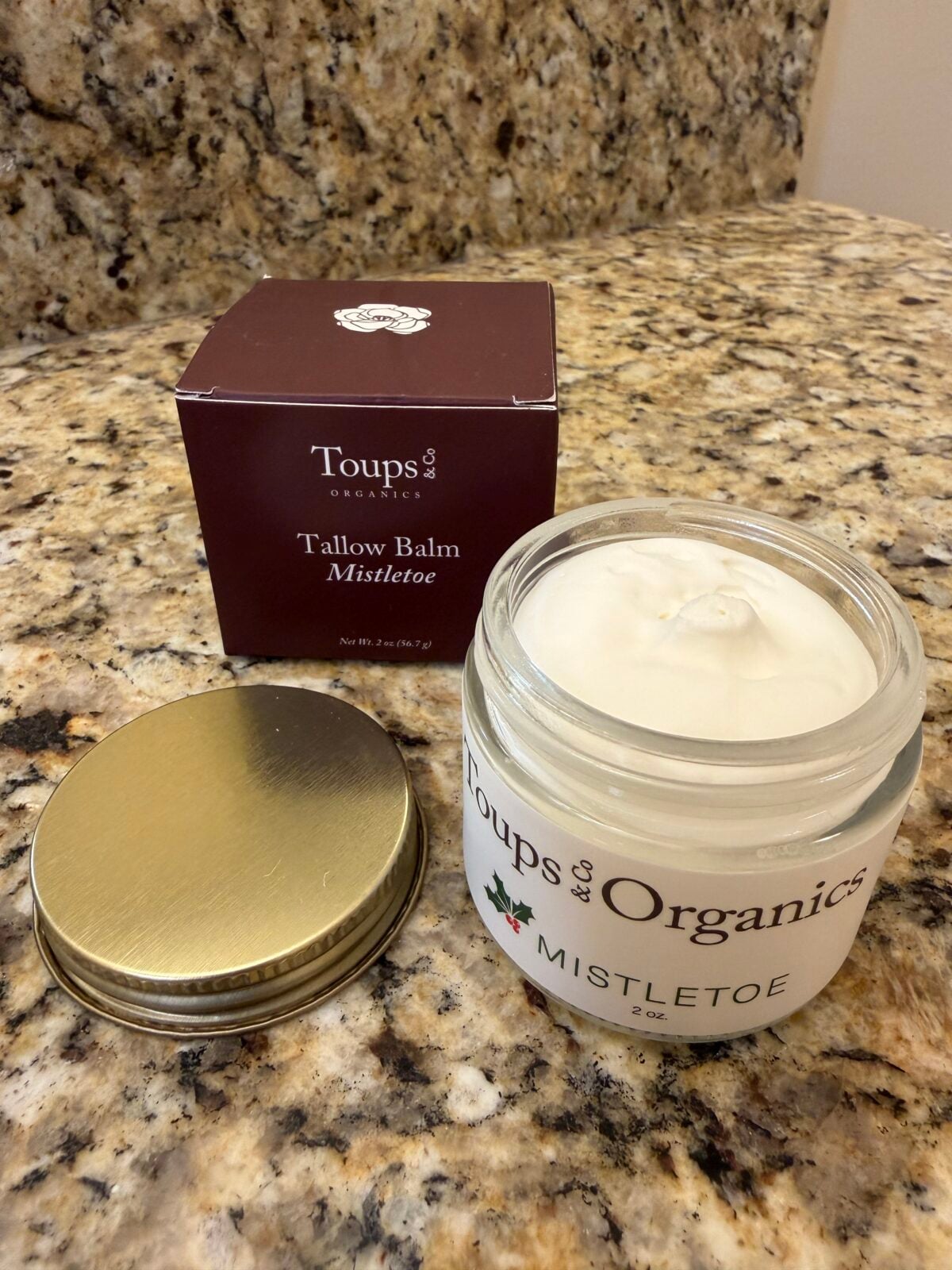 Toups & Organics Mistletoe Tallow Balm in clear glass jar with brown box on granite counter