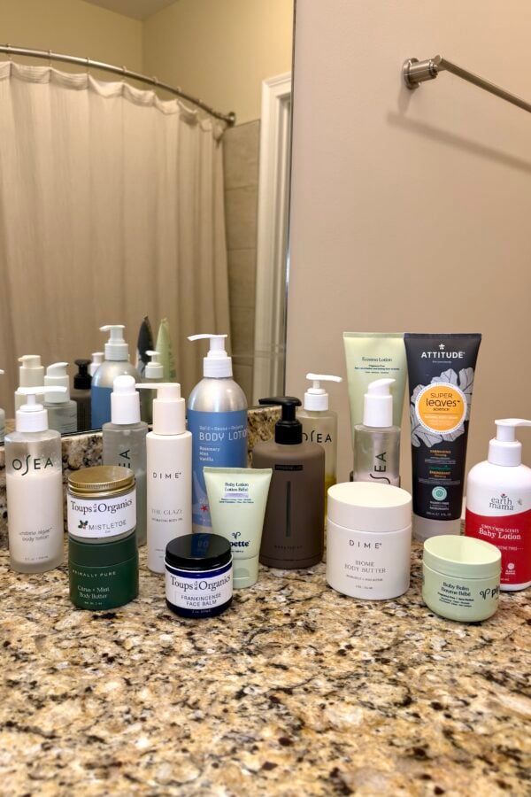 Assortment of natural body care products including brands like Osea, Dime, Attitude, and Earth Mama arranged on granite bathroom countertop