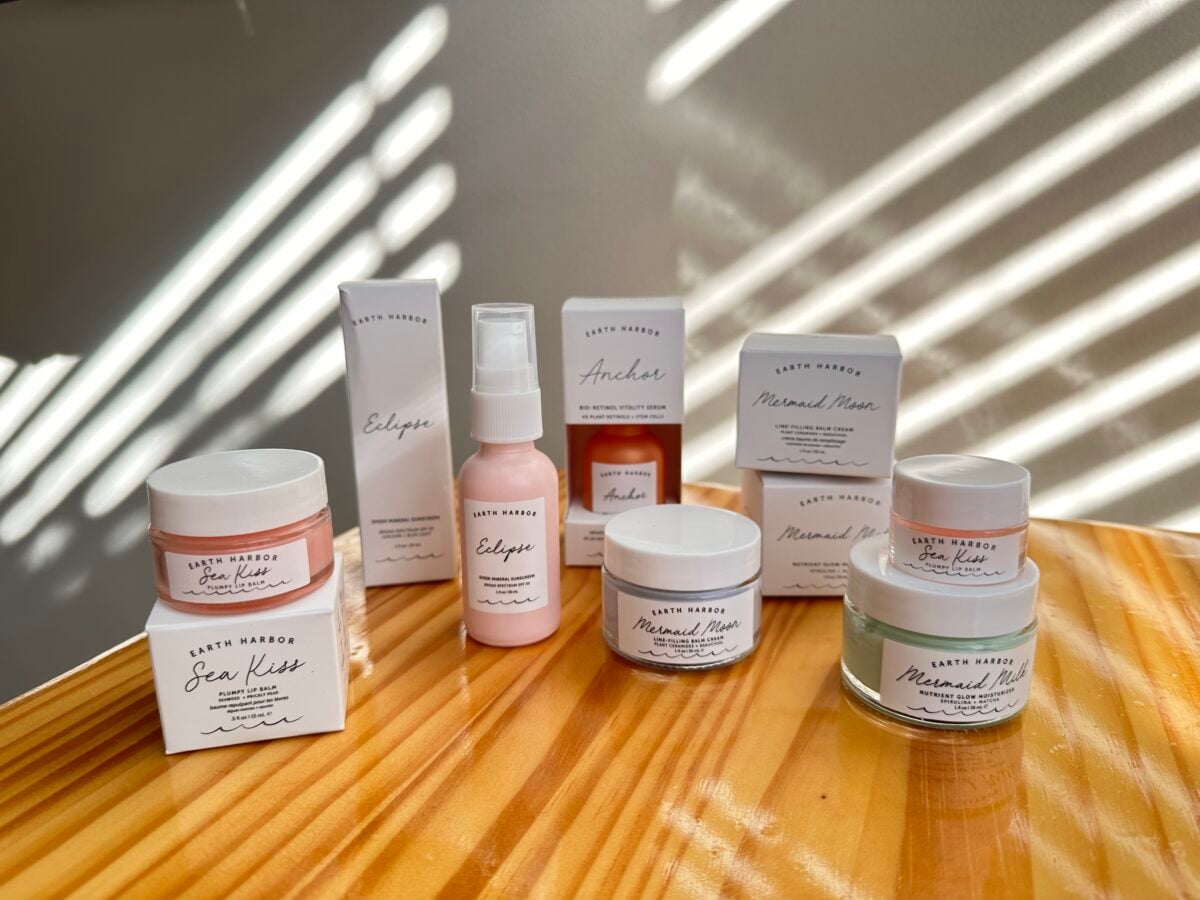 Earth Harbor skincare products including Sea Kiss lip scrub, Eclipse mist, Anchor serum, and Mermaid Milk cream displayed on wooden surface with natural light