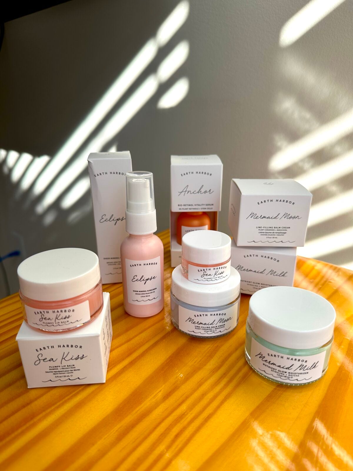 Earth Harbor skincare products including Sea Kiss lip scrub, Eclipse mist, Anchor serum, and Mermaid Milk cream displayed on wooden surface with natural light