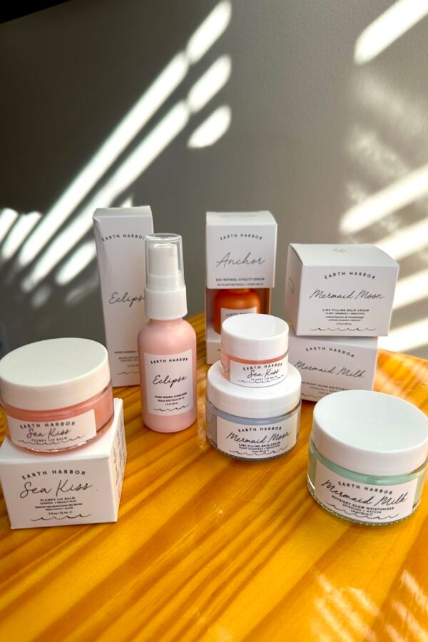 Earth Harbor skincare products including Sea Kiss lip scrub, Eclipse mist, Anchor serum, and Mermaid Milk cream displayed on wooden surface with natural light