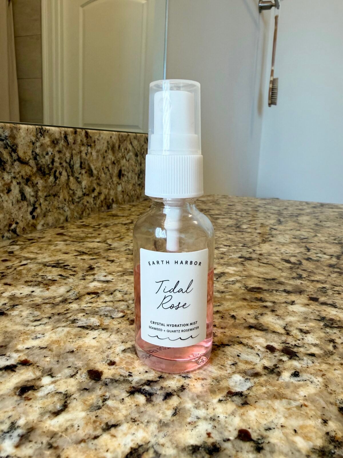 The photo shows a clear glass spray bottle of Earth Harbor "Tidal Rose" Crystal Hydration Mist, filled with a pink liquid, sitting on a speckled granite countertop.