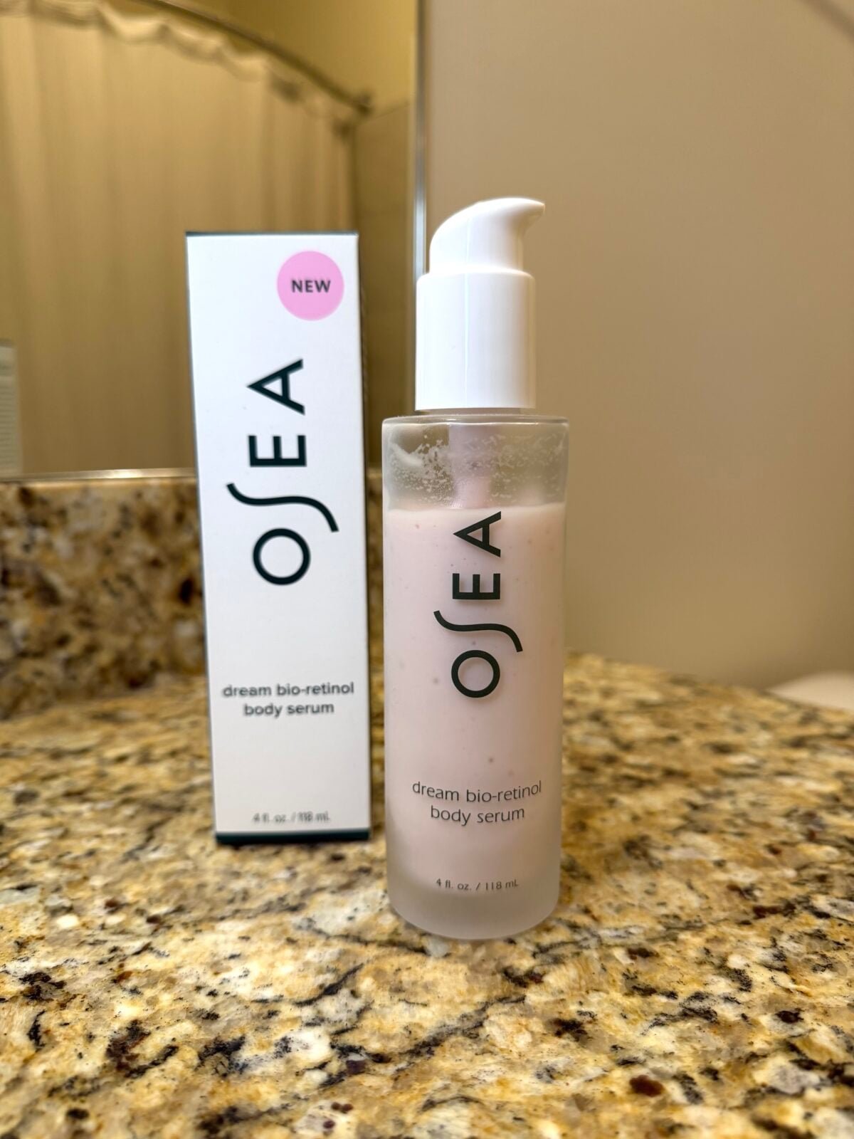 A 4 fl. oz. frosted glass pump bottle of OSEA "dream bio-retinol body serum" sits next to its white cardboard packaging on a granite bathroom countertop.