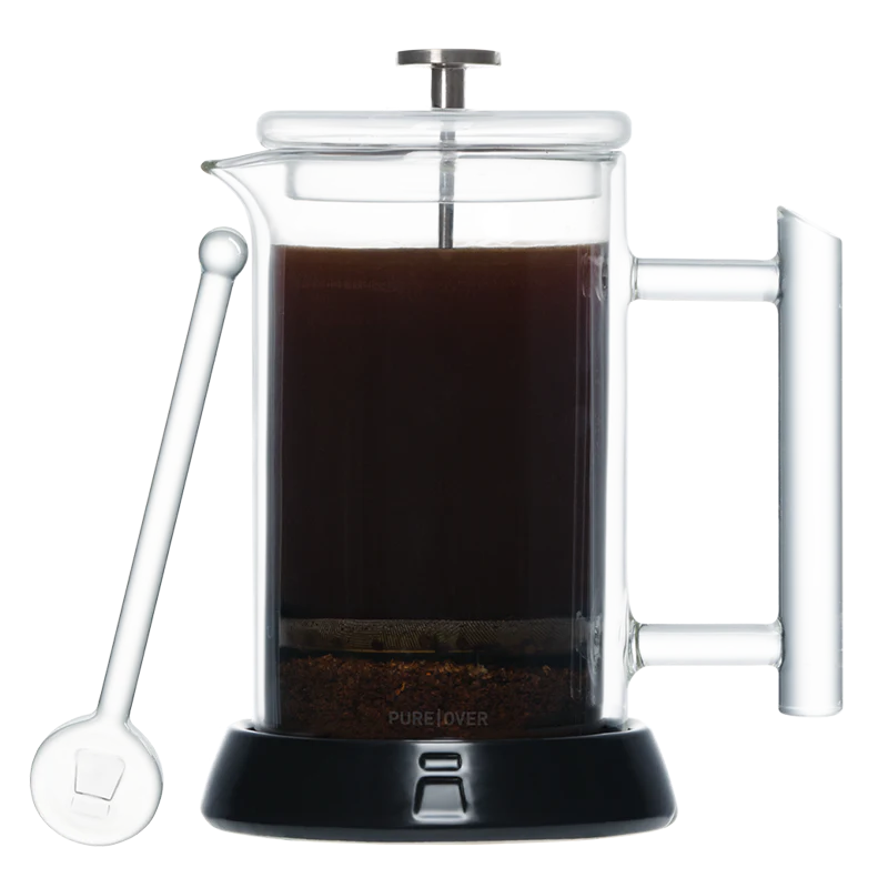 The photo shows a clear glass Pure Over coffee maker filled with brewed coffee and a layer of grounds at the bottom, standing next to a glass stirring rod.