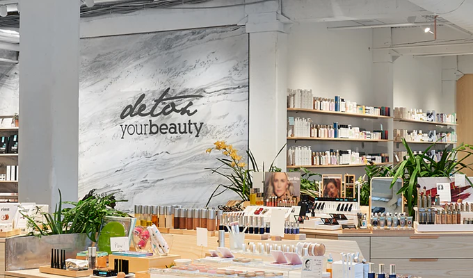 The photo features the interior of a beauty store with "detox your beauty" written on a marble-patterned wall, surrounded by various skincare and cosmetic products on wooden shelves and displays.