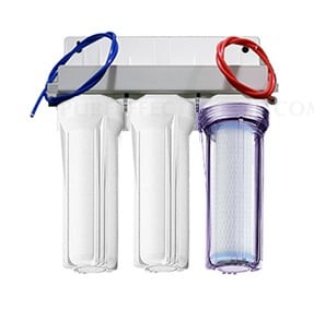 The image shows a three-stage under-sink water filtration system consisting of two solid white filter housings and one clear housing that reveals a internal filter, accompanied by blue and red connection tubing.