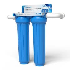 The image displays a SpringWell dual-cartridge water filtration system featuring two large blue filter housings connected to white PVC piping against a plain white background.