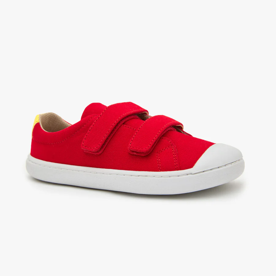 A red childrens sneaker with two Velcro straps, a white rubber sole, and a small yellow detail on the heel, shown against a plain white background.
