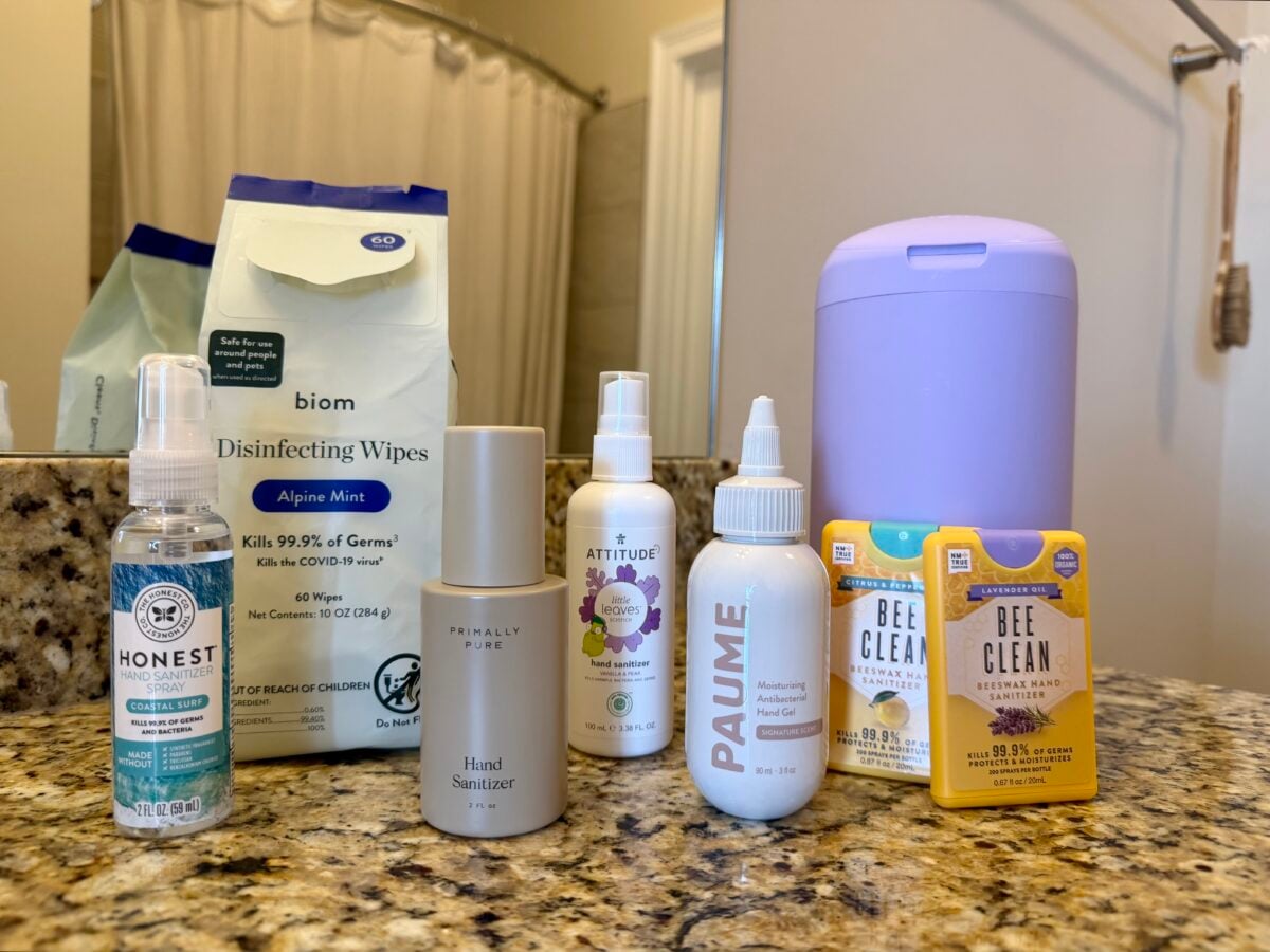 A granite bathroom counter holds disinfecting wipes, a blue container, two yellow Bee Clean soap bars, Honest hand sanitizer, Primally Pure sanitizer, Attitude mist, and Paume moisturizing hand sanitizer.