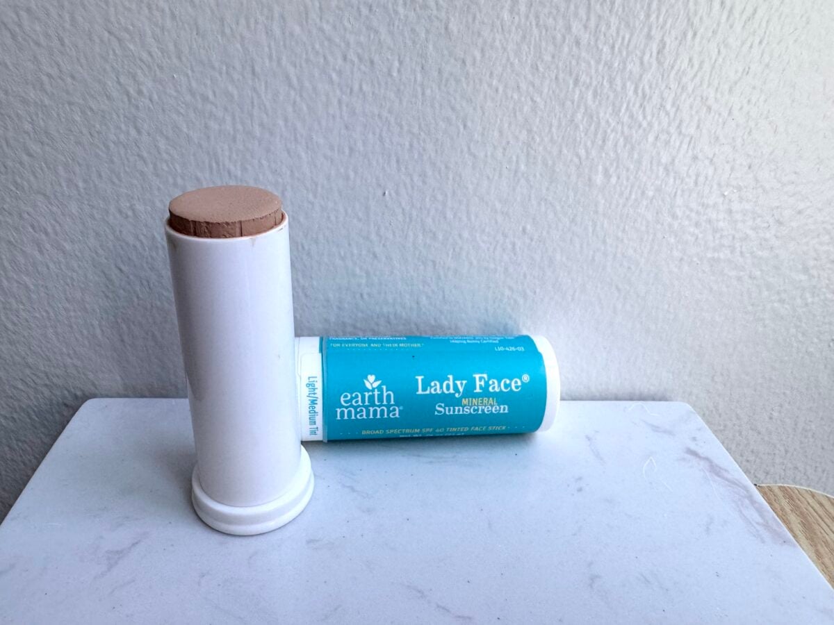 A tube of Earth Mama Lady Face SPF 40 mineral sunscreen stick, partially opened to show the tan product, sits on a white surface against a light gray wall.