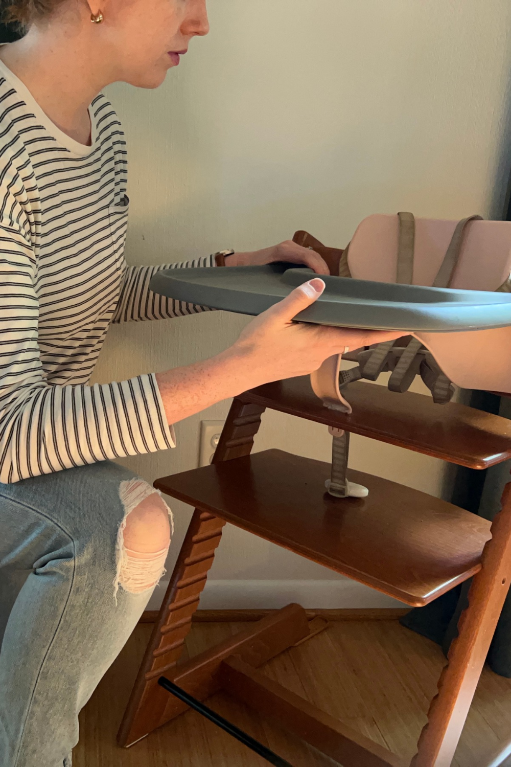 A person attaches a gray plastic tray to a wooden high chair.