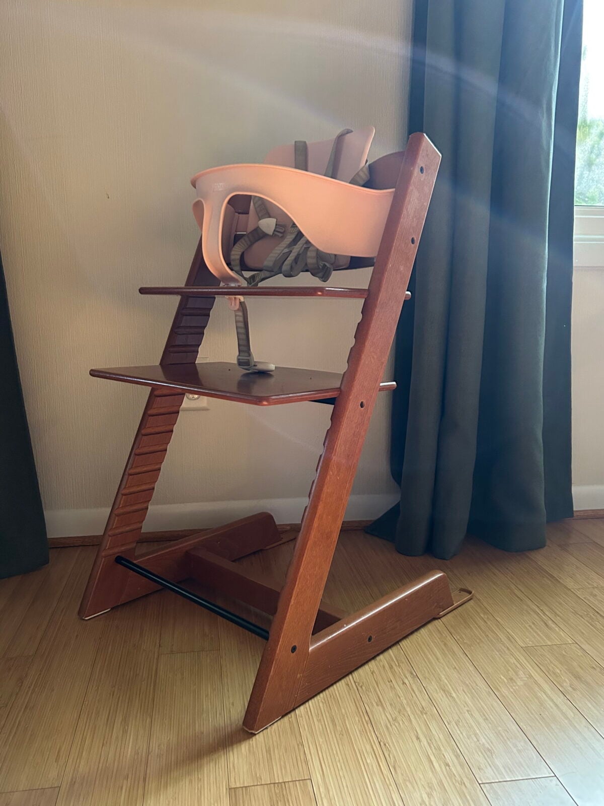 Wooden adjustable high chair with a pink plastic seat and harness.