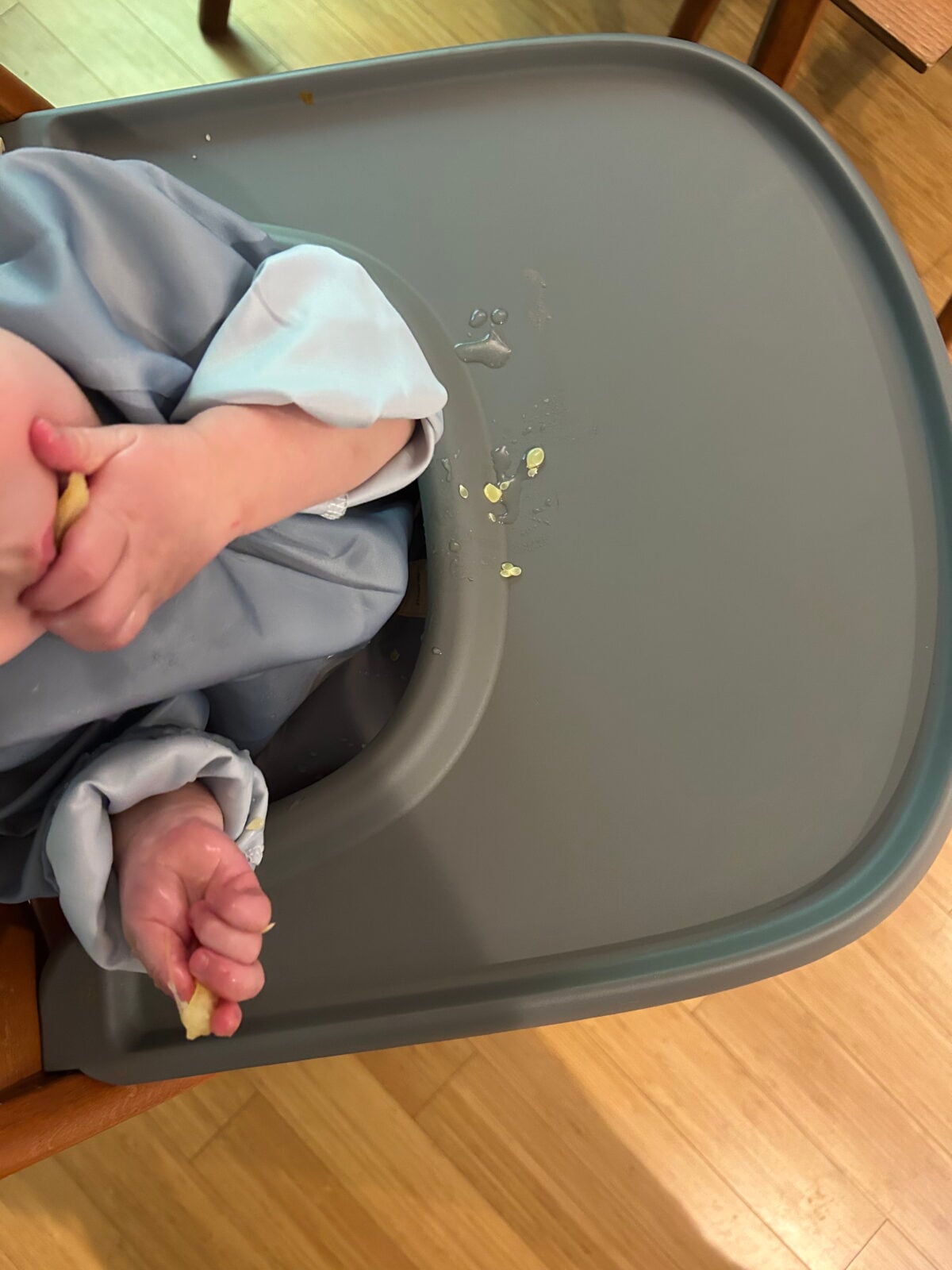 A baby sitting in a high chair with food pieces and droplets on the tray.
